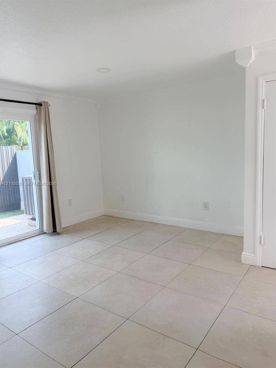 Recessed lighting, crown molding, white walls, light-toned tile flooring, and a sliding glass door