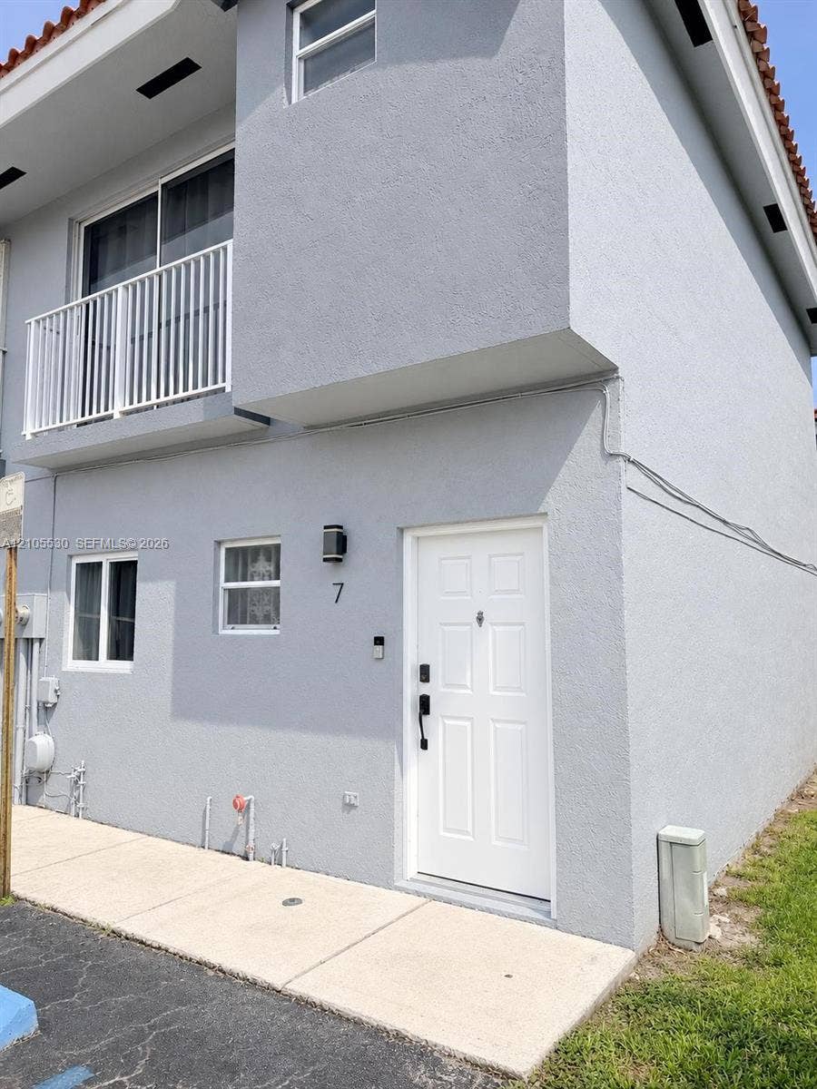Two-story stucco exterior with a tiled roof, white paneled entry door, and a second-story balcony with white railings
