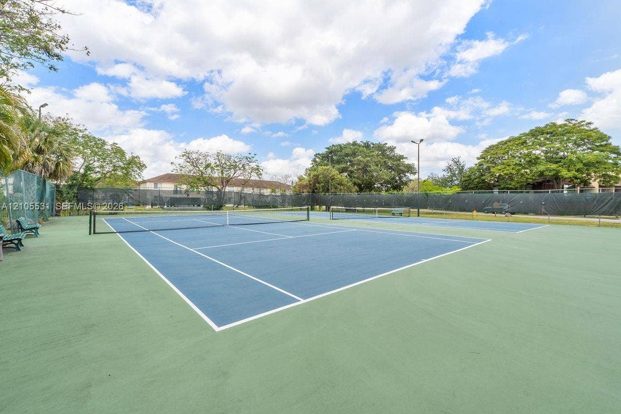 Two tennis courts featuring blue and green playing surfaces, surrounded by green fencing