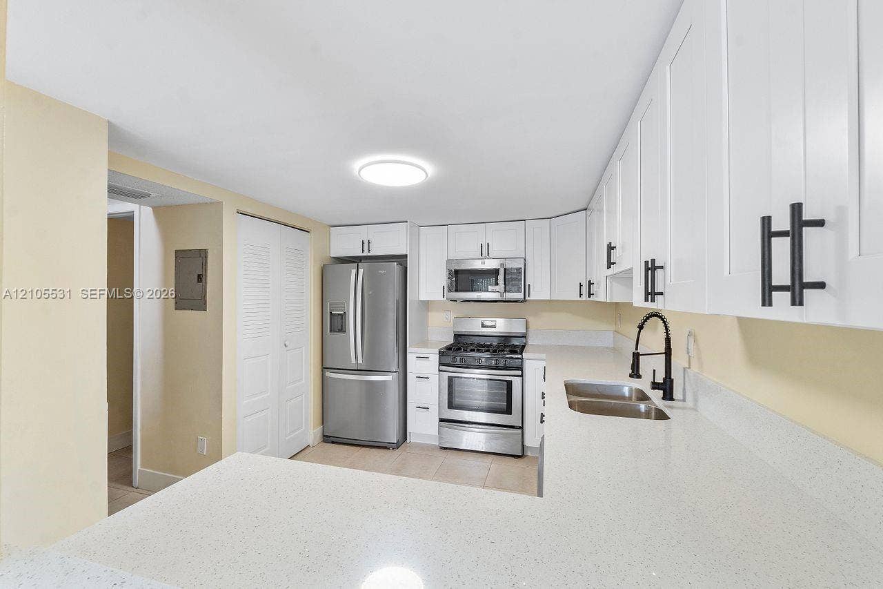 Contemporary kitchen featuring white cabinetry, stainless steel appliances, light-toned countertops, a matte black faucet, and a stainless steel sink