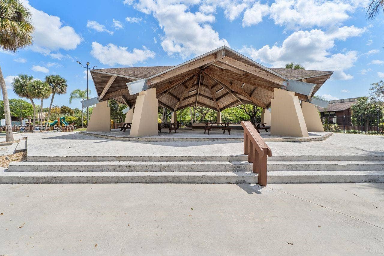 Expansive concrete patio with tiered steps, leading to a covered pavilion featuring a wood-beam ceiling, sturdy support pillars, and integrated picnic tables