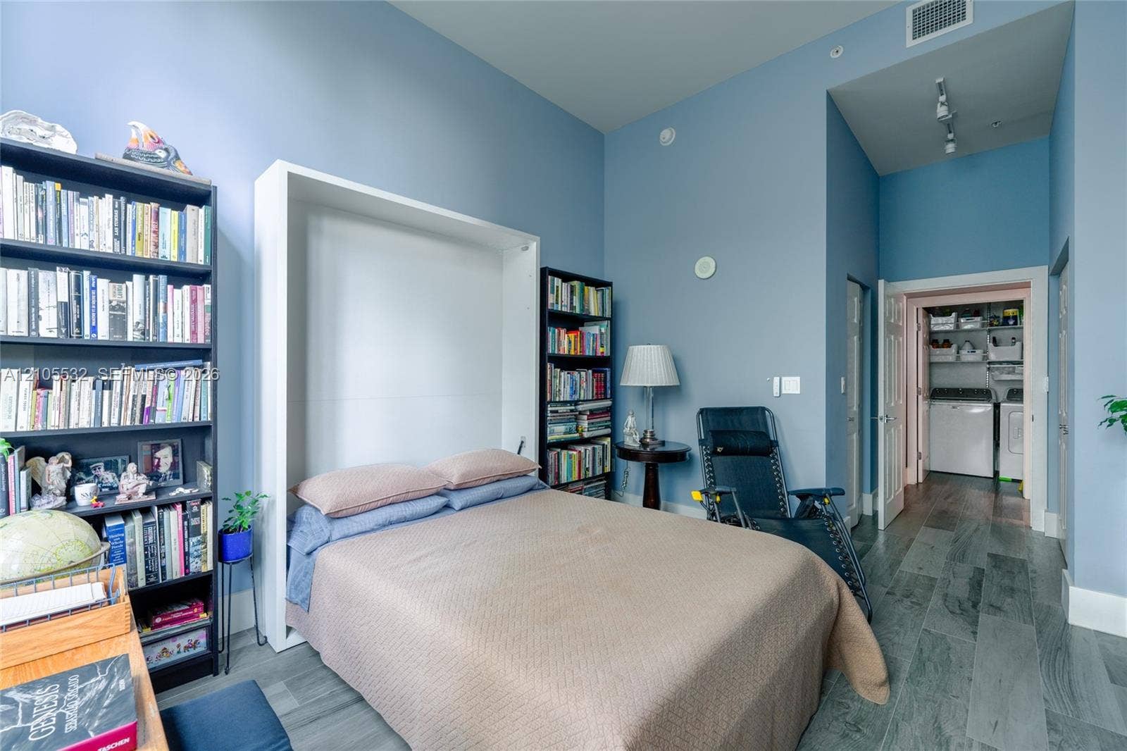 High-ceiling interior featuring a built-in Murphy bed, wood-finish flooring, and recessed ceiling lighting