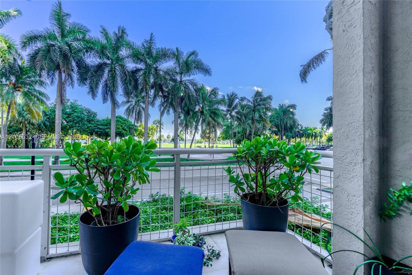Covered balcony with white metal lattice railing, tiled flooring, and mature palm tree scenery