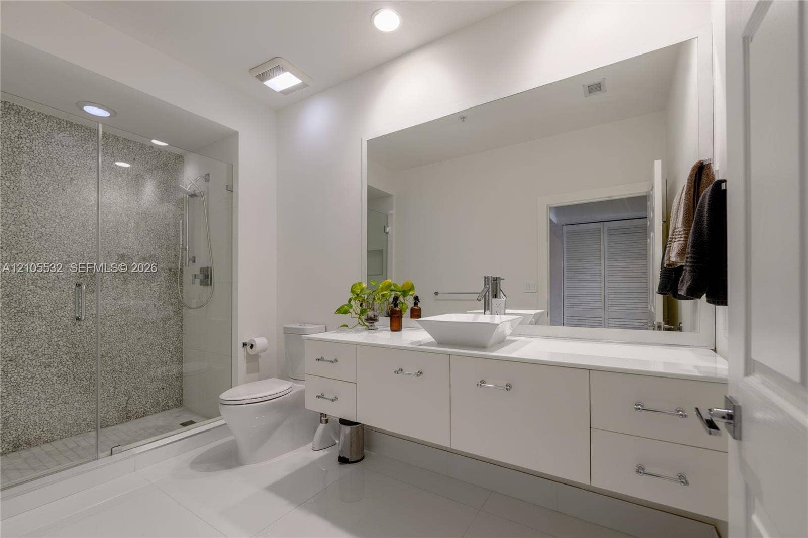 Floating white vanity with a rectangular vessel sink, solid-surface countertop, frameless glass shower enclosure, and textured stone-finish shower wall