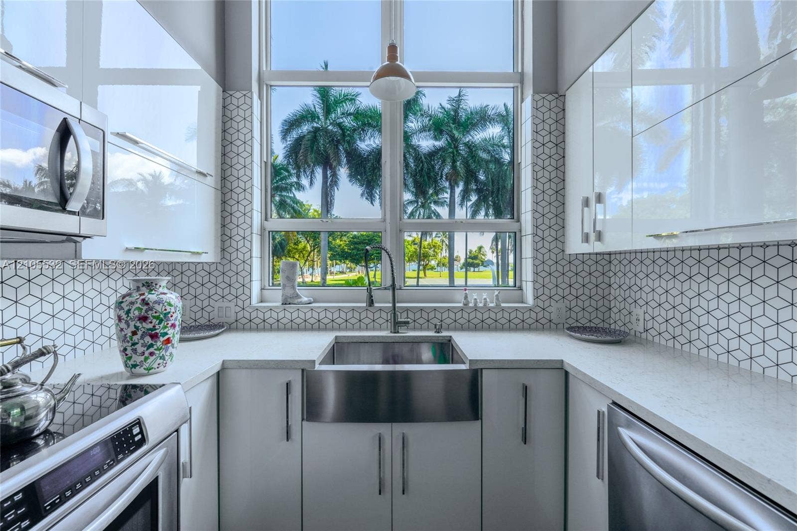 Kitchen featuring high-gloss cabinetry, stone-finish countertops, stainless steel farmhouse sink, and geometric-patterned backsplash tile, accented by a floor-to-ceiling window