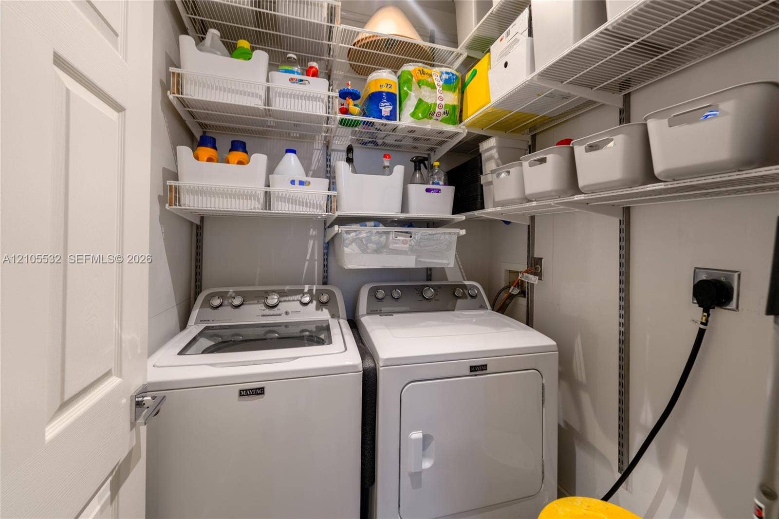 Laundry area featuring white top-load washer and dryer, multi-tier white wire shelving, and an integrated electrical outlet