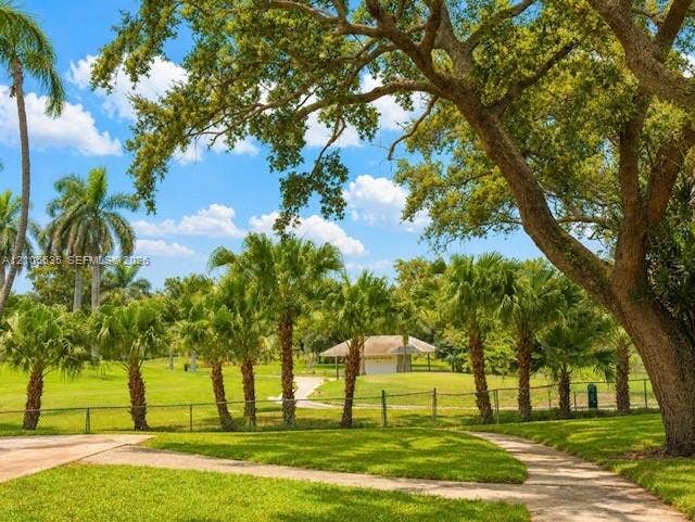 Expansive green space featuring a paved walkway, mature trees, and a distant building with a covered patio