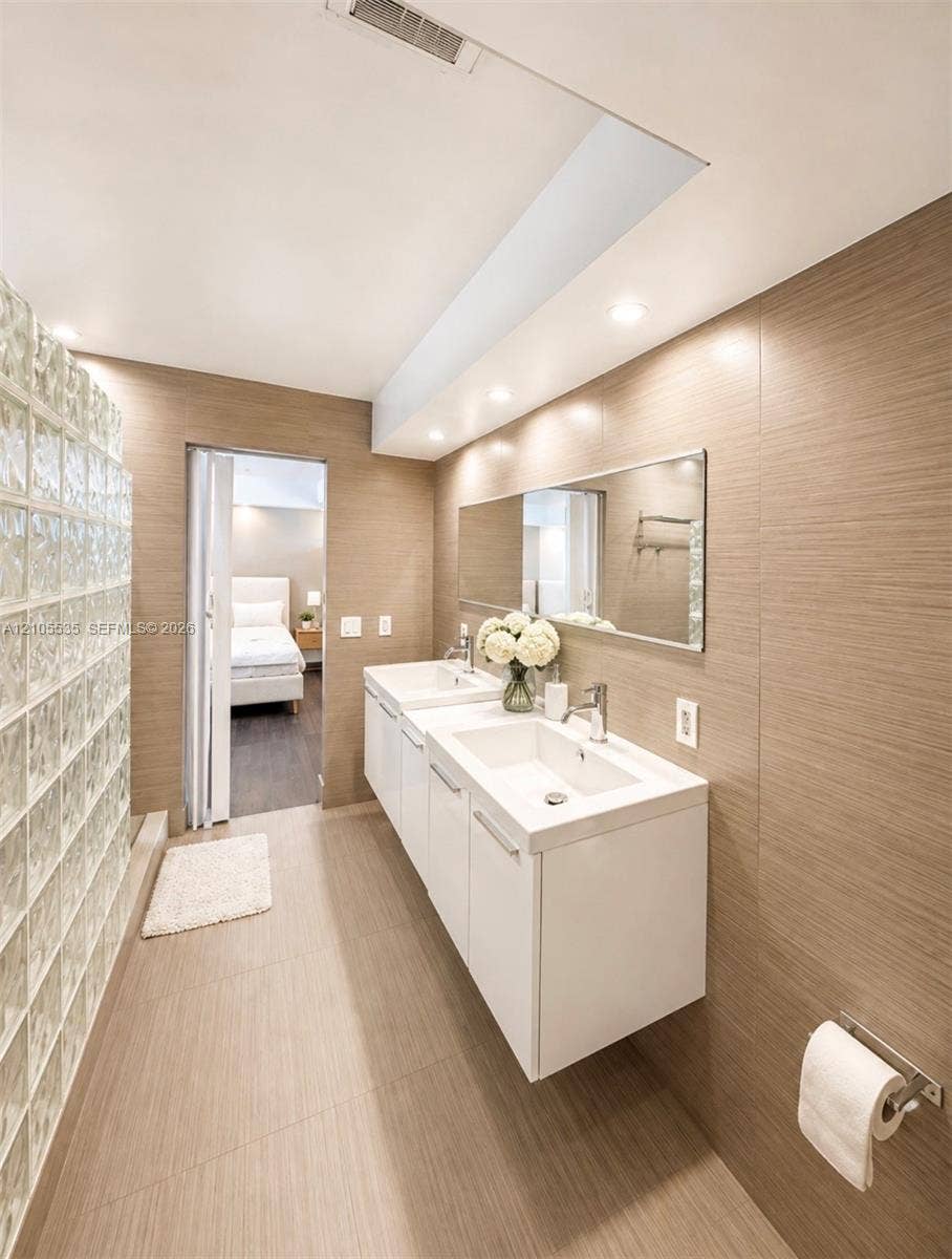 Dual floating vanities with integrated sinks, recessed lighting, glass block wall, and large wall-mounted mirror