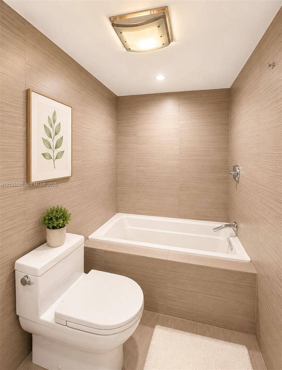 White built-in bathtub with chrome fixtures, surrounded by neutral-toned wall tiles