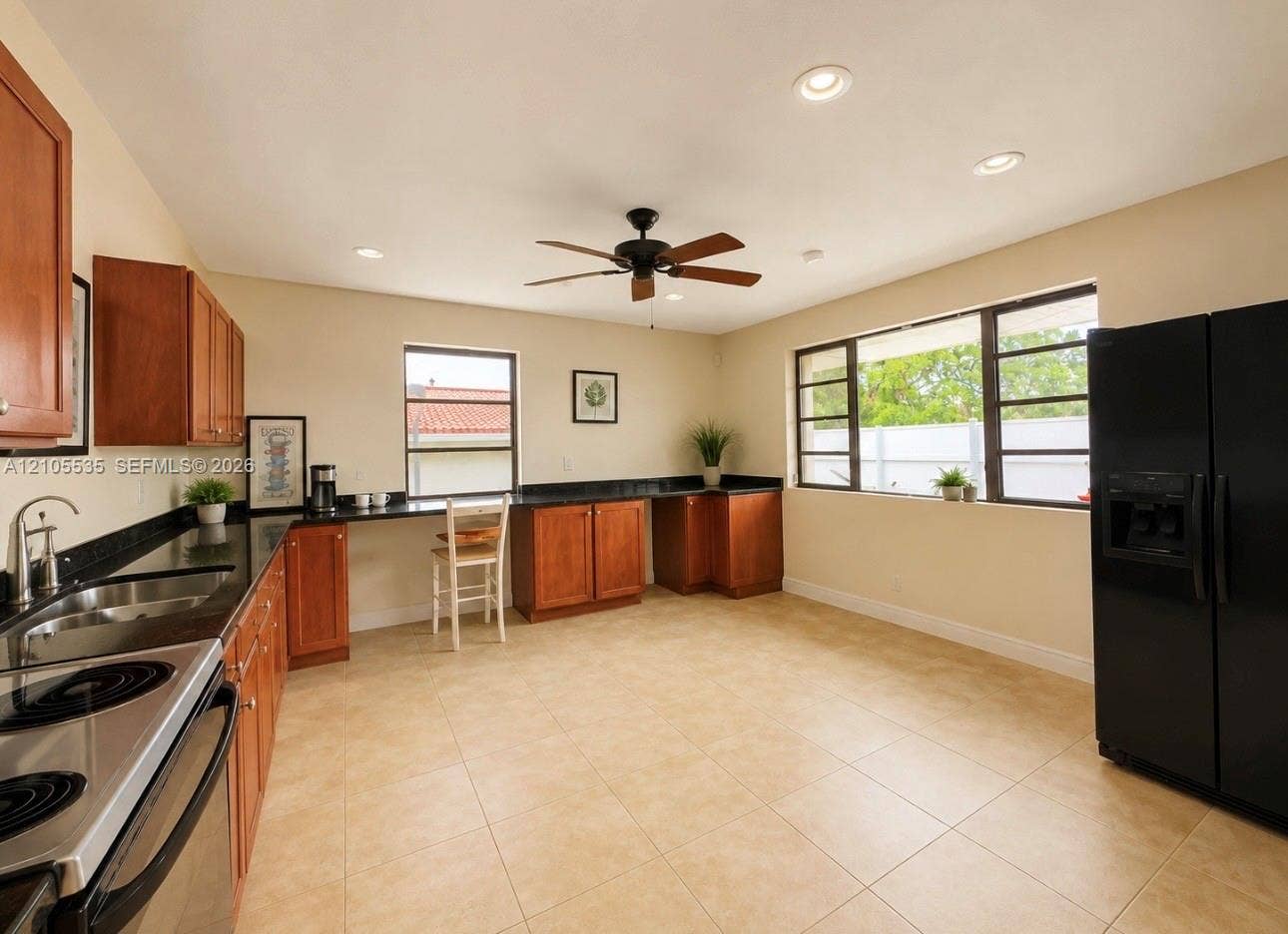 Kitchen featuring tile flooring, wood cabinetry, dark countertops, a stainless steel range, and a black refrigerator