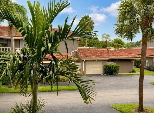 Stucco exterior featuring a terracotta tile roof, attached garage, and mature landscaping