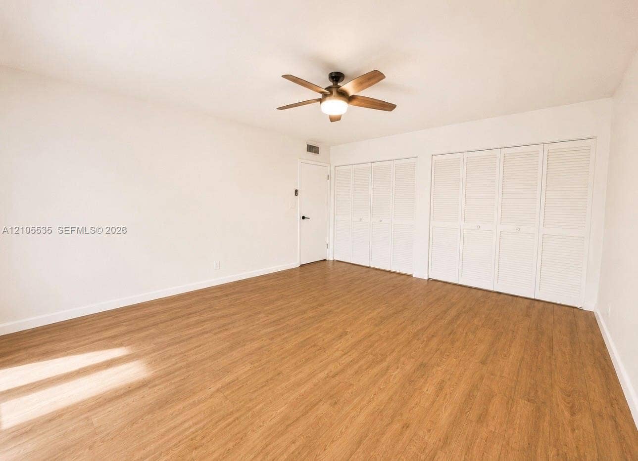 Wood-finish flooring, ceiling fan with integrated lighting, and multiple louvered bifold closet doors