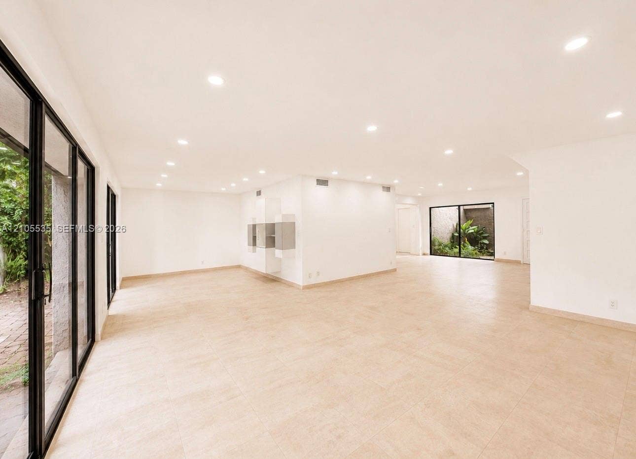 Spacious interior with neutral tile flooring, recessed lighting, expansive glass doors, and built-in shelving units