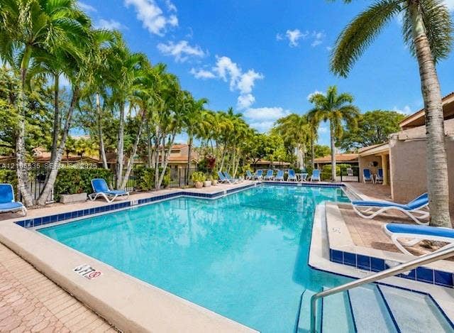 Outdoor swimming pool with tiled border and integrated steps, surrounded by mature palm trees and a paved deck