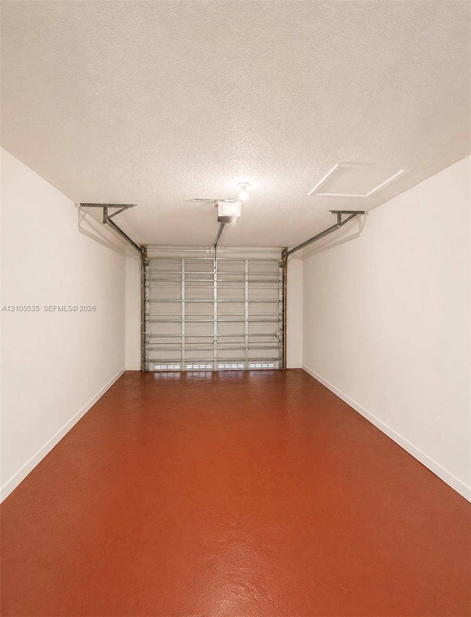 Garage with a sealed concrete floor, automatic garage door opener, and a ceiling-mounted light fixture