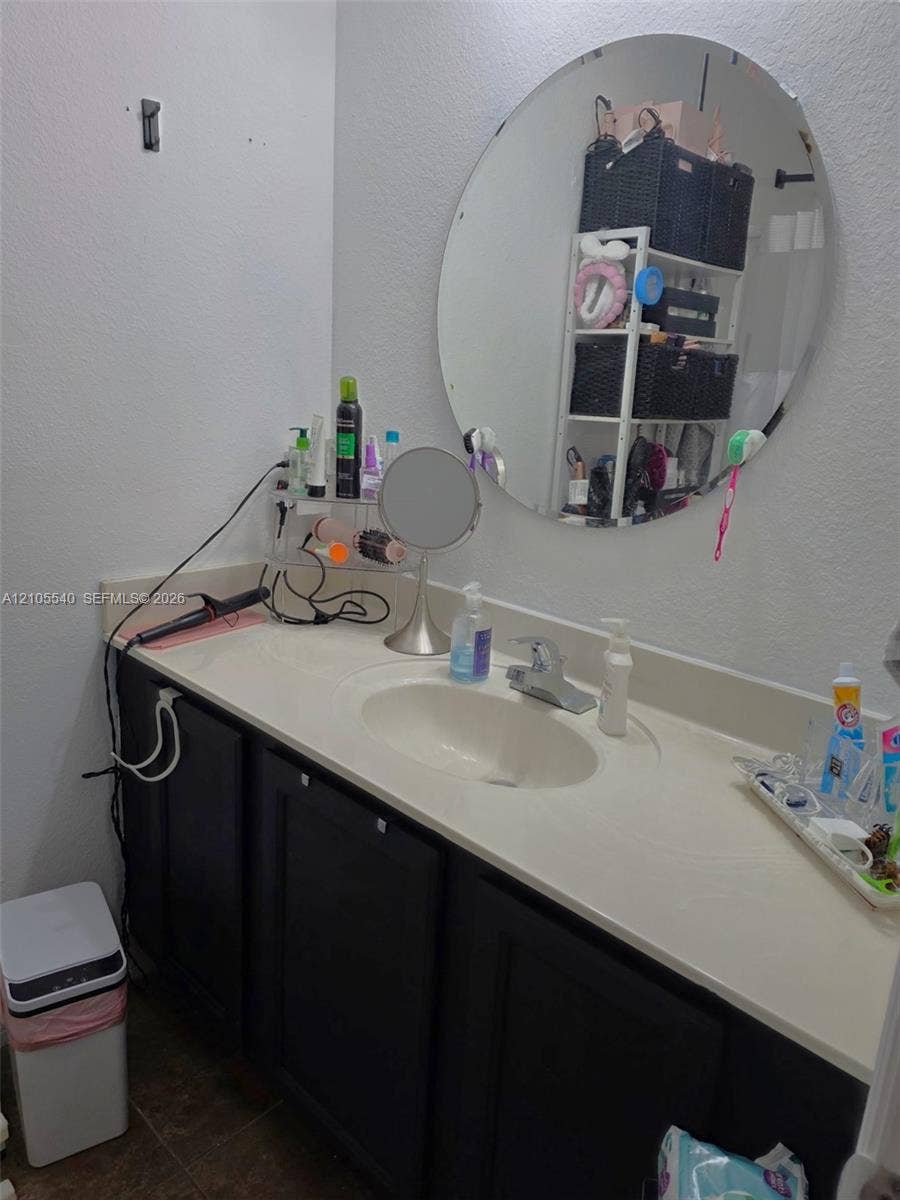 21935 SW 102nd Avenue, Cutler Bay, FL 33190 Single vanity with integrated sink, dark wood-finish cabinetry, and a circular wall-mounted mirror