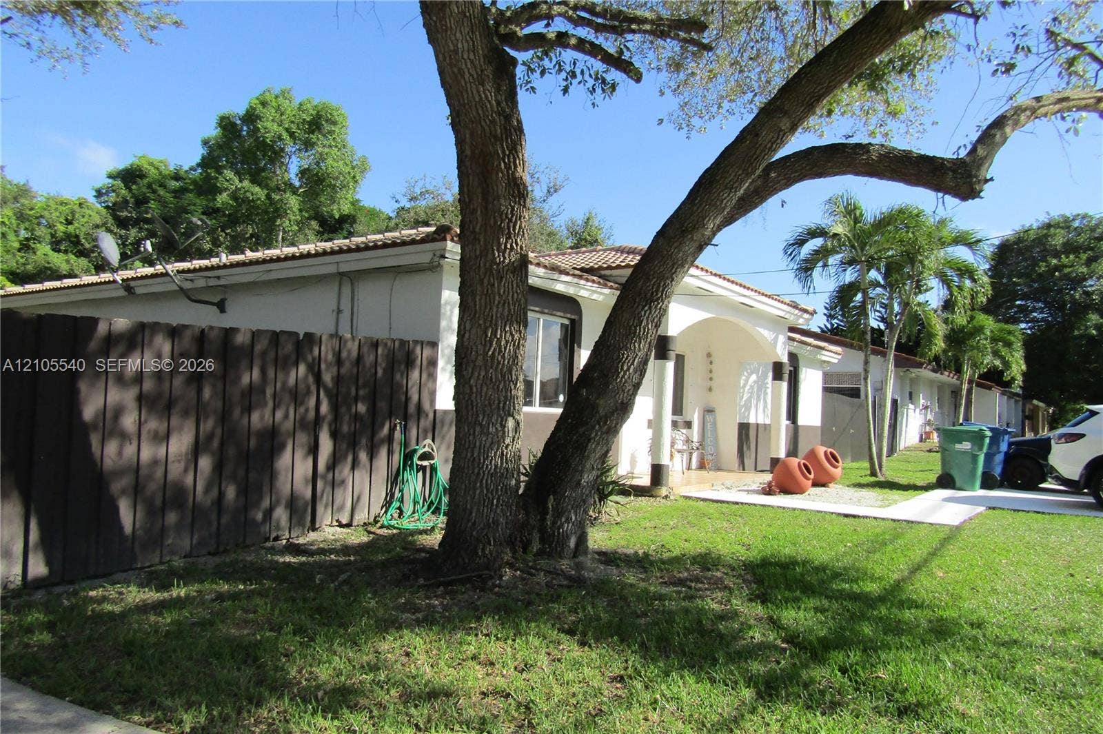 21935 SW 102nd Avenue, Cutler Bay, FL 33190 Manicured front lawn with mature trees, a white stucco exterior, dark wood fencing, and a tiled roof