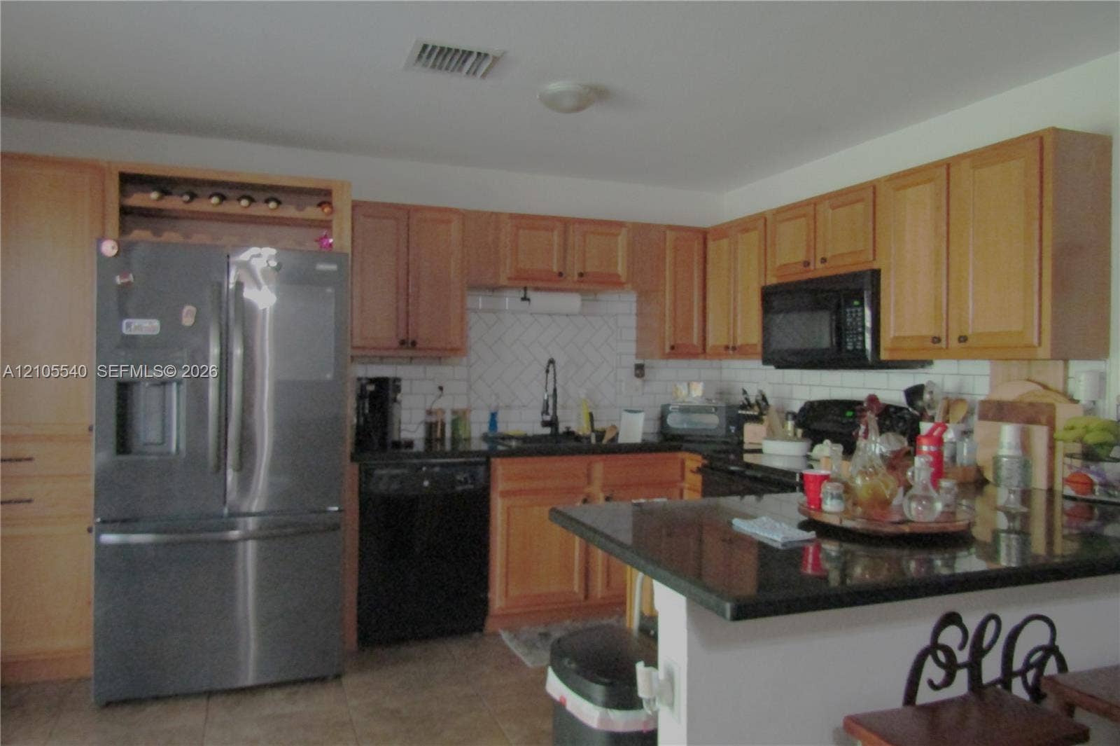 21935 SW 102nd Avenue, Cutler Bay, FL 33190 Kitchen featuring wood cabinetry, a built-in wine rack, stainless steel refrigerator, black appliances, and a dark stone countertop on the island