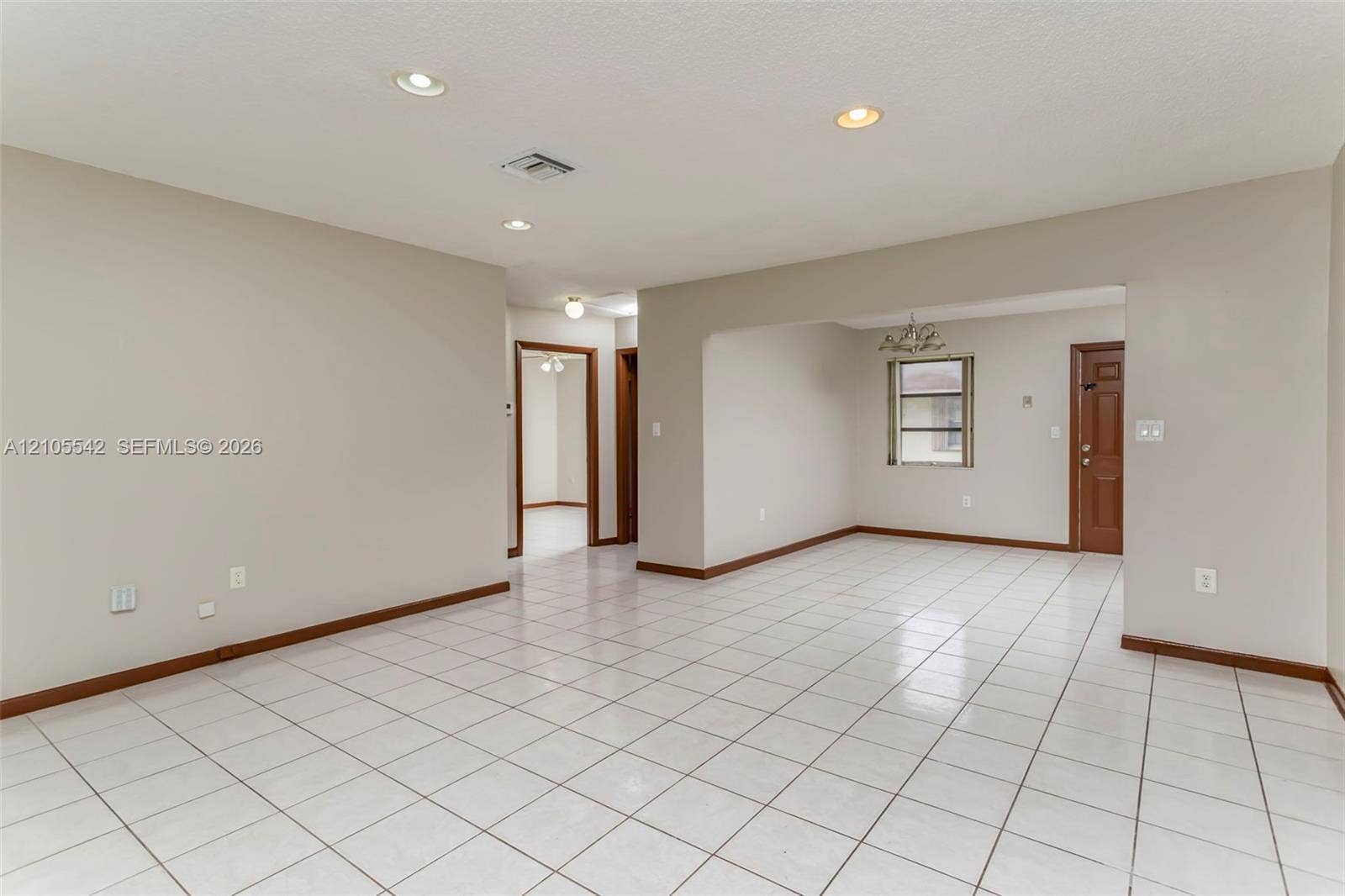 Spacious room featuring white tile flooring, recessed lighting, neutral wall tones, and wood-finish trim
