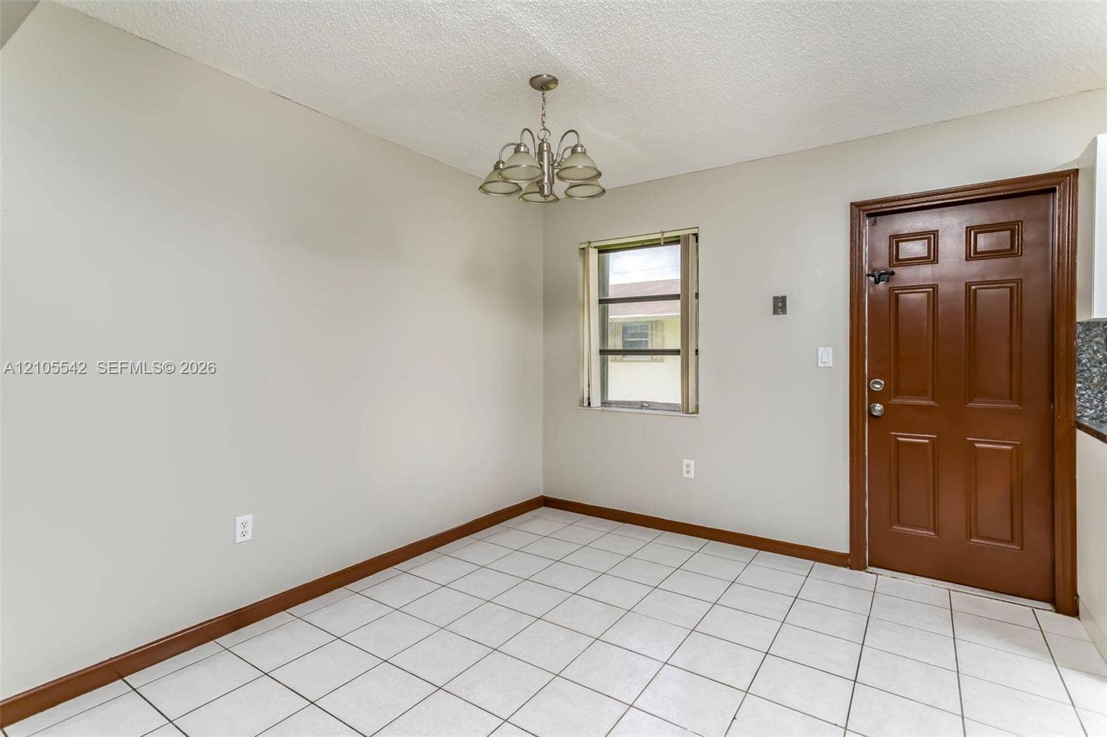 White square tile flooring, neutral wall paint, single-pane window, solid panel door, and ceiling-mounted light fixture