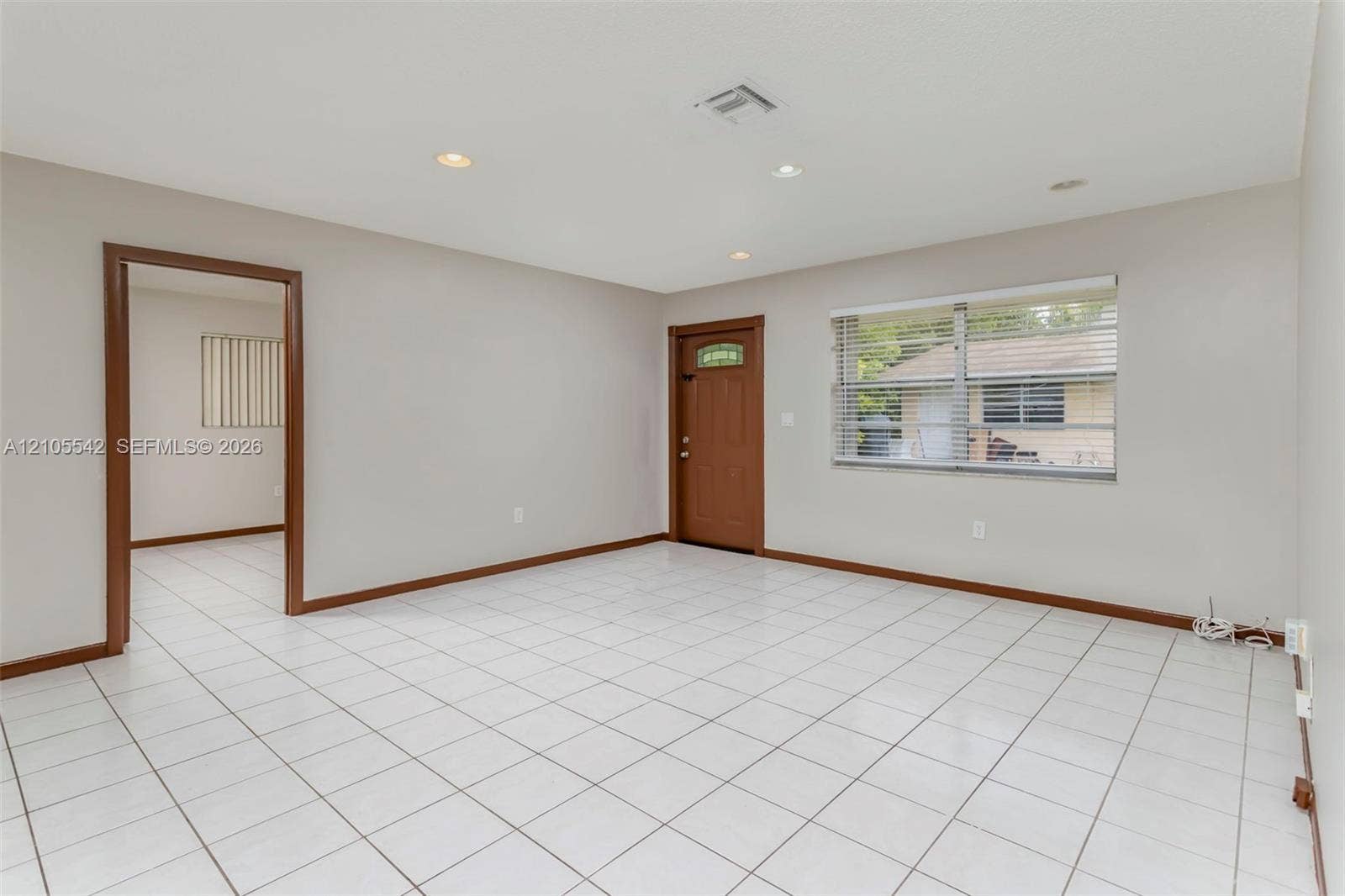 White tile flooring, recessed lighting, and a wood-finish entry door with clear glass panel