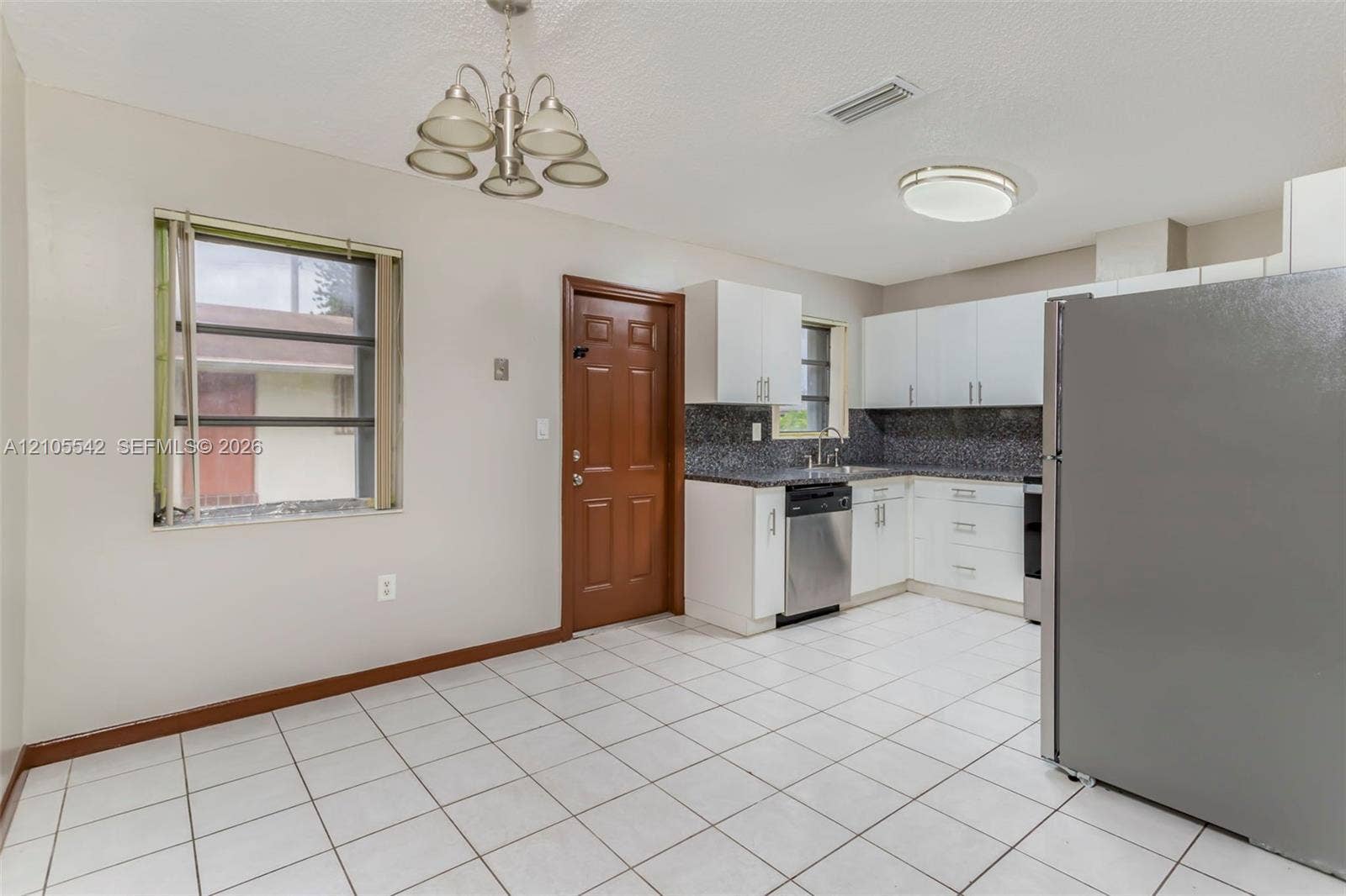 Tile flooring, white cabinetry, granite-finish countertops, stainless steel appliances, and a brown paneled door