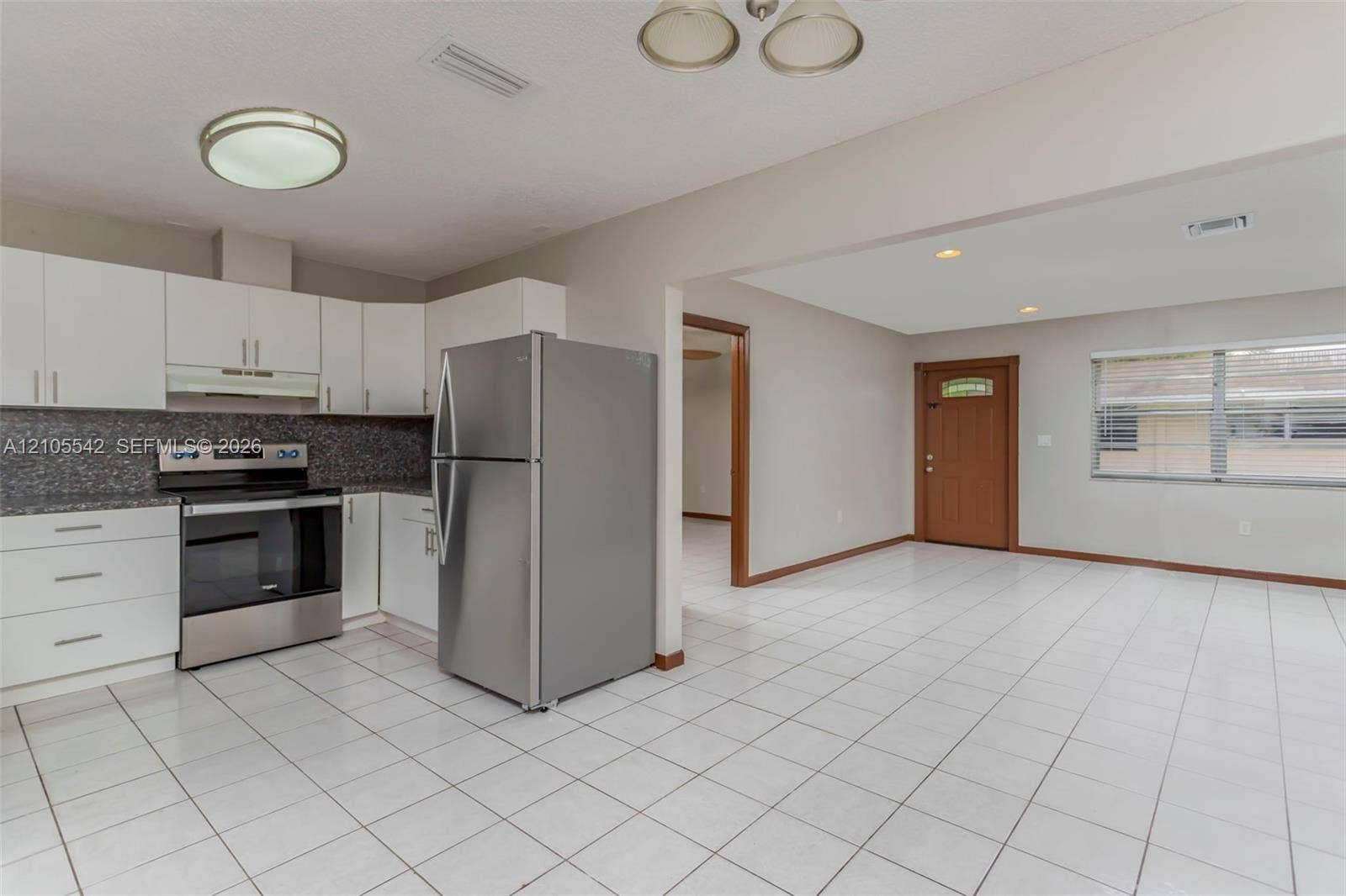 Kitchen featuring white cabinetry, stainless steel appliances, dark speckled countertops, and white tile flooring