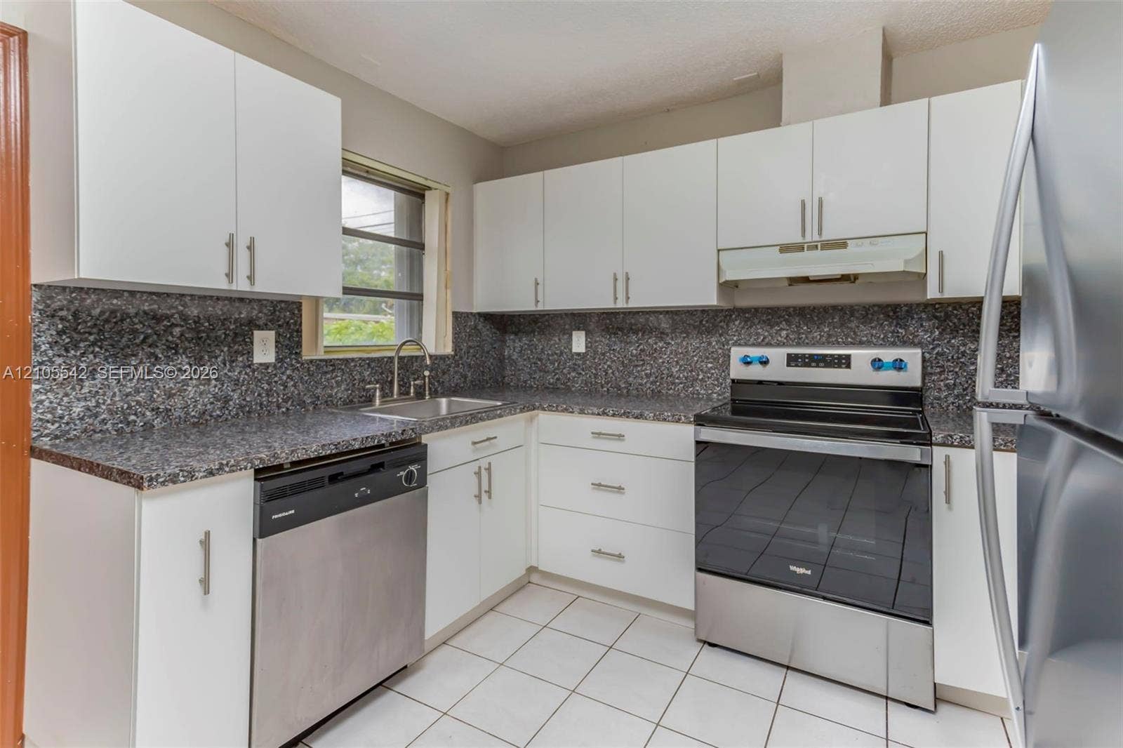 Kitchen featuring white cabinetry, dark speckled countertops, stainless steel appliances, and white tile flooring