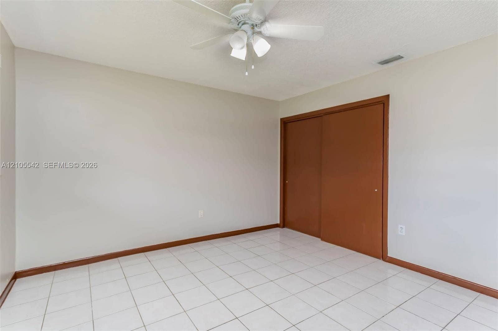 White tile flooring, light neutral wall paint, ceiling fan light fixture, and brown sliding closet doors