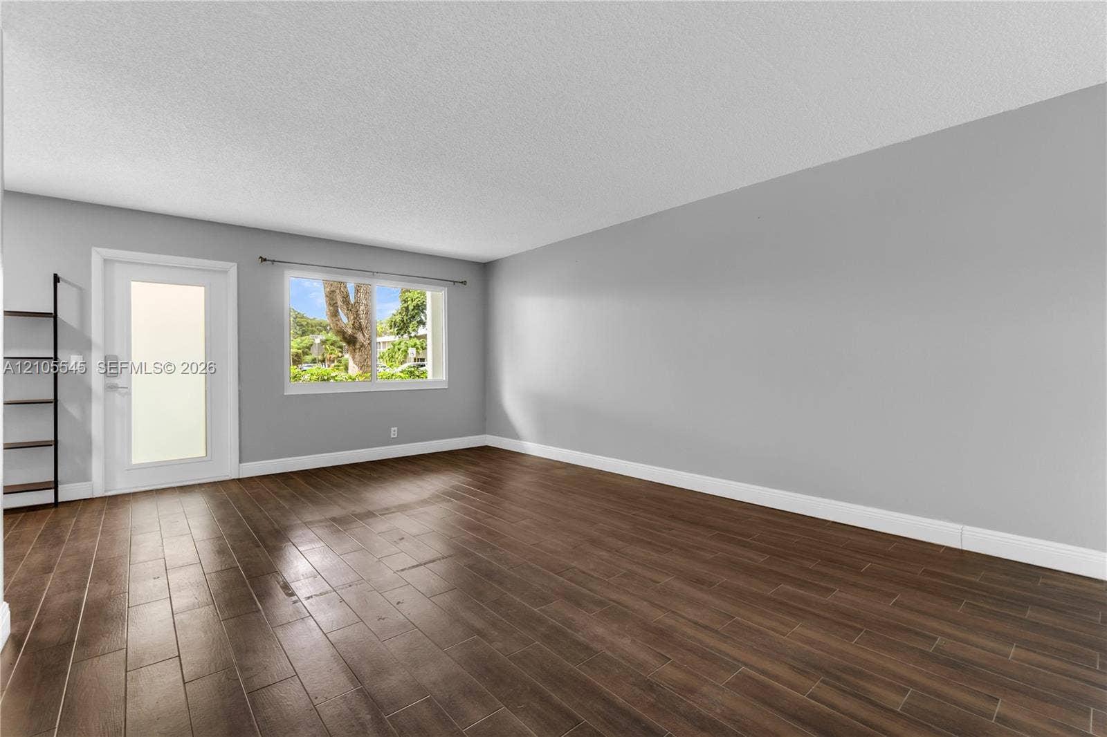 222 Tilford A, #222, Deerfield Beach, FL 33442 Wood-finish plank tile flooring, light gray painted walls, a large window, a glass-paneled door, and a built-in shelving unit