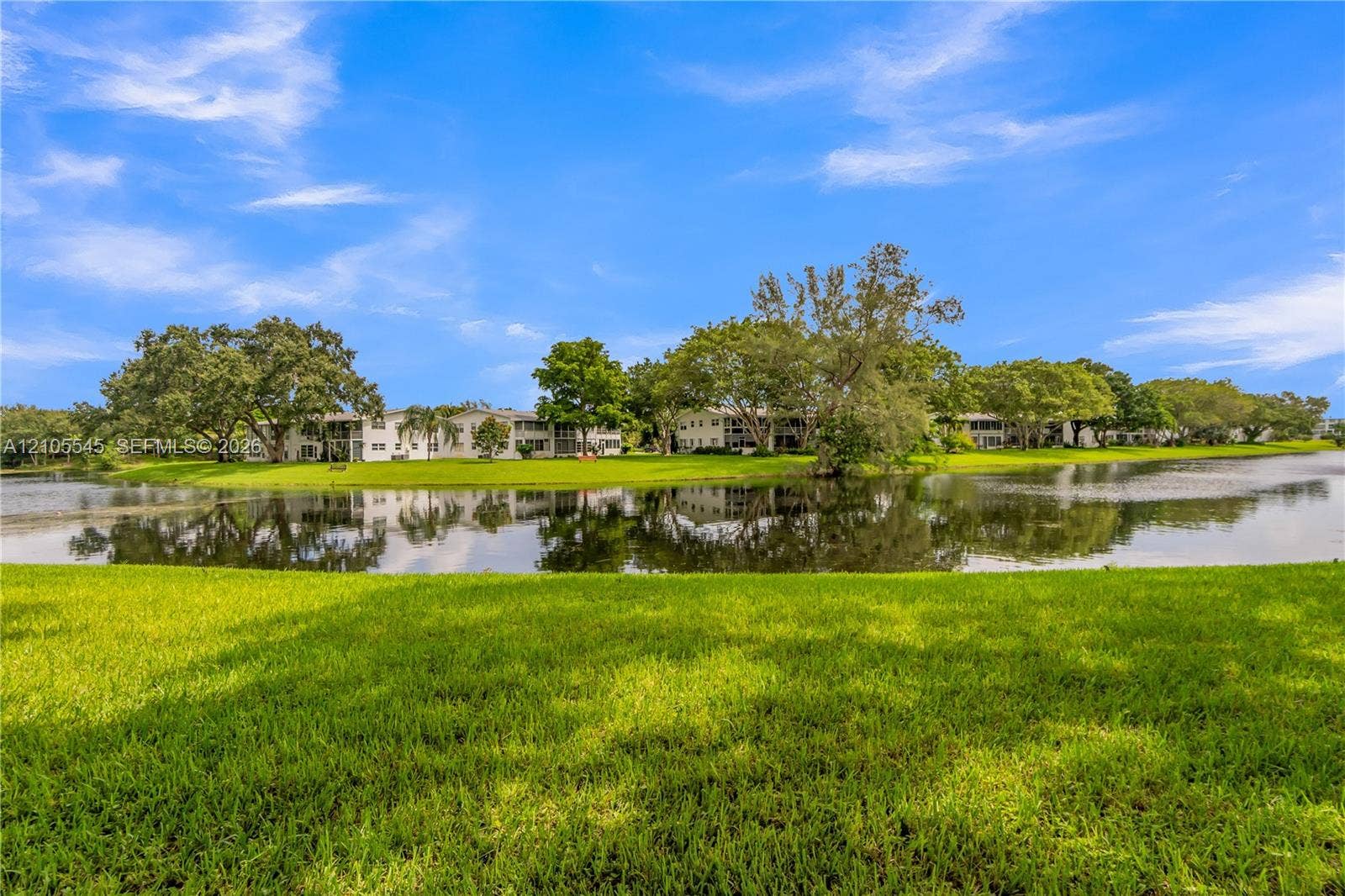 222 Tilford A, #222, Deerfield Beach, FL 33442 Expansive green lawn bordering a reflective body of water with established trees and multiple residential buildings in the background