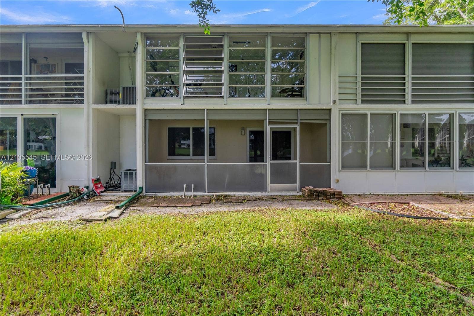 222 Tilford A, #222, Deerfield Beach, FL 33442 Screened patio with a white framed door, sliding glass doors, upper-level windows, and a grassy outdoor area