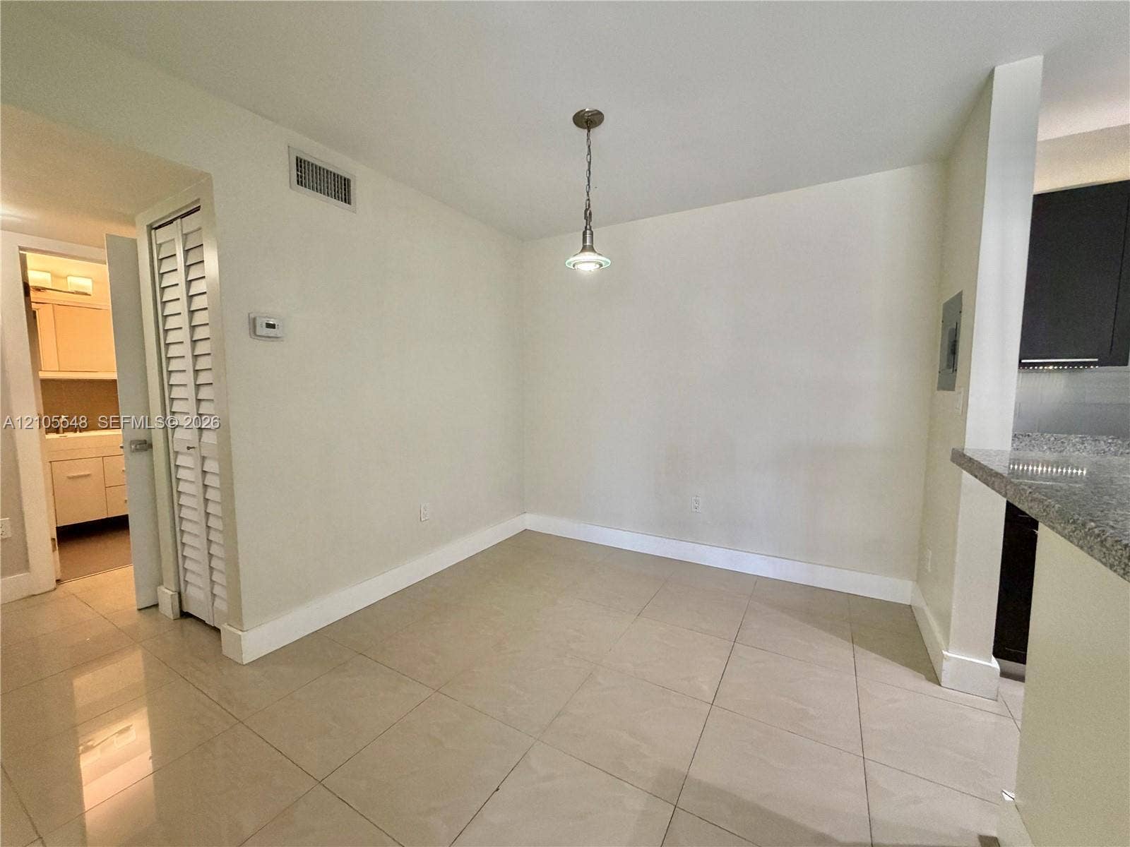 Neutral-toned large format tile flooring, single-pendant light fixture, and closet with louvered double doors