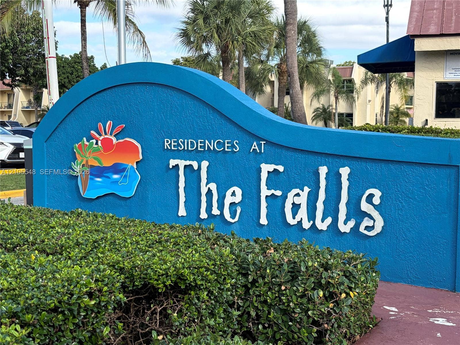 Monument signage for Residences at The Falls featuring a blue stucco finish, dimensional lettering, and mature landscaped shrubbery