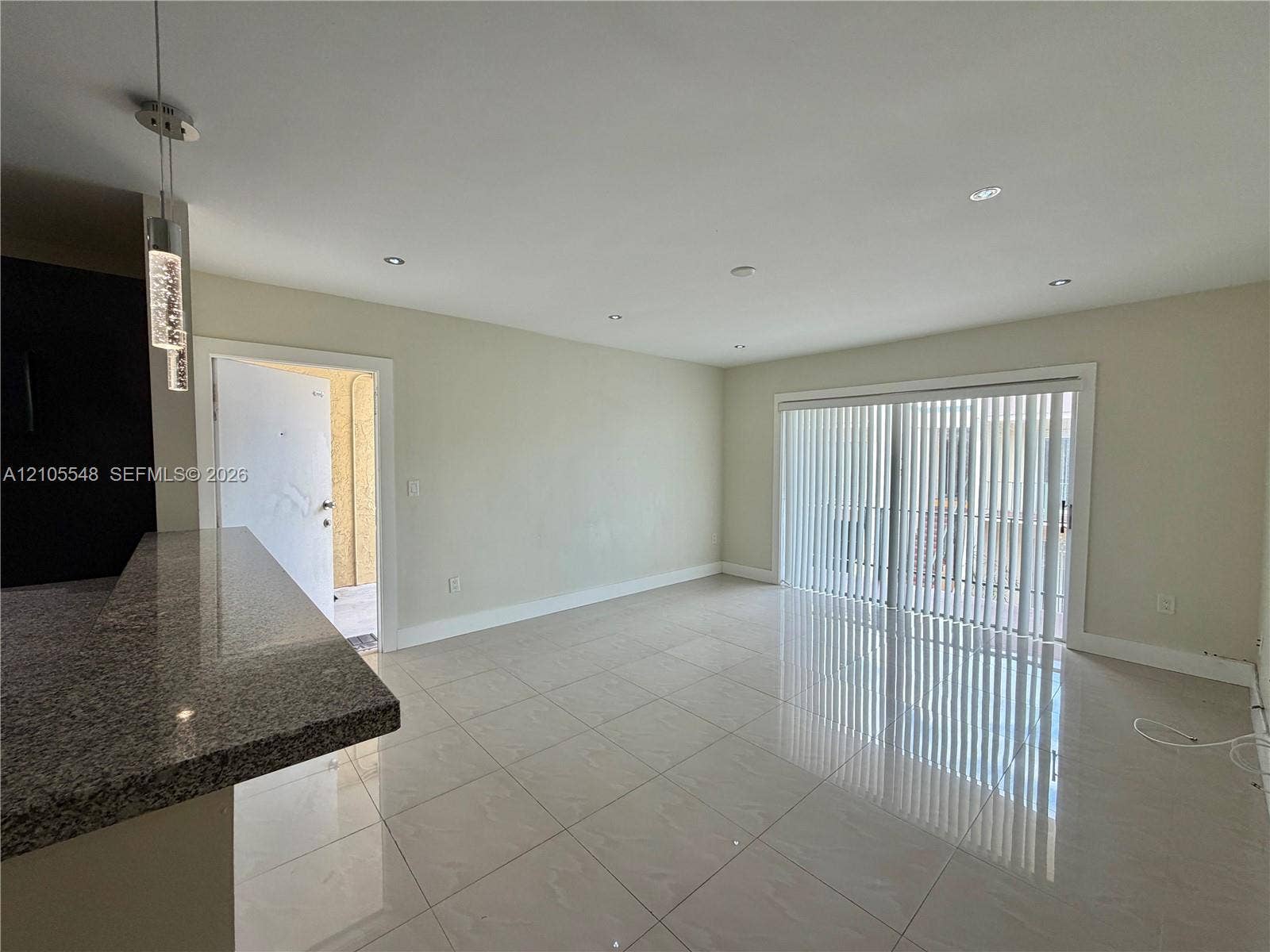 Polished tile flooring, recessed lighting, granite breakfast bar, and sliding glass doors with vertical blinds