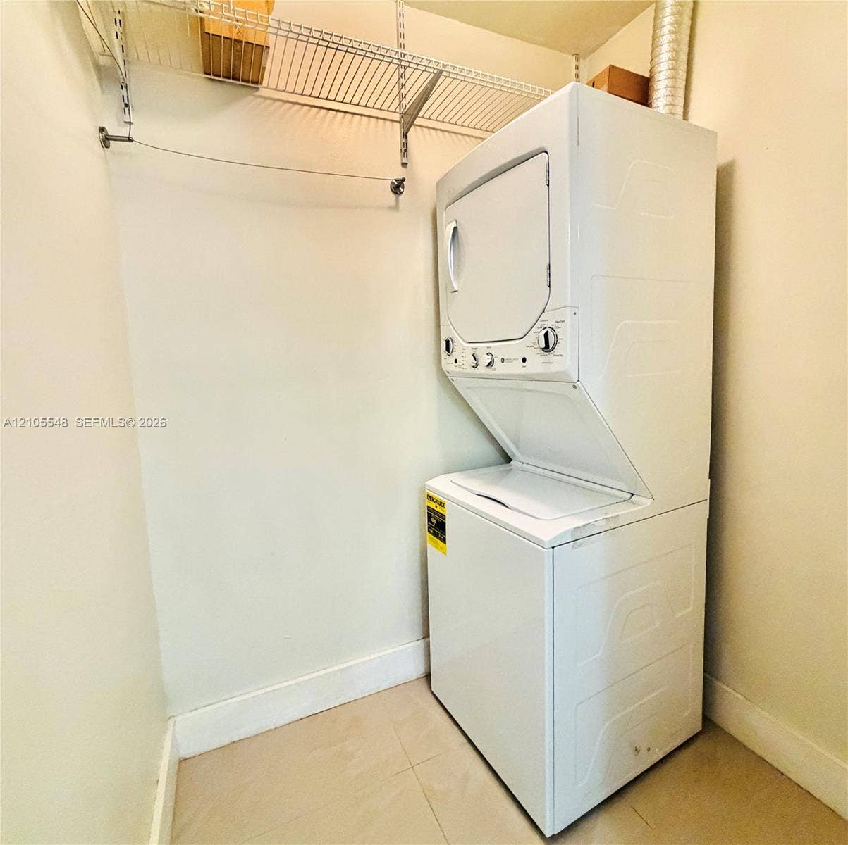 Laundry area featuring a stacked washer and dryer unit, neutral tile flooring, and overhead wire shelving