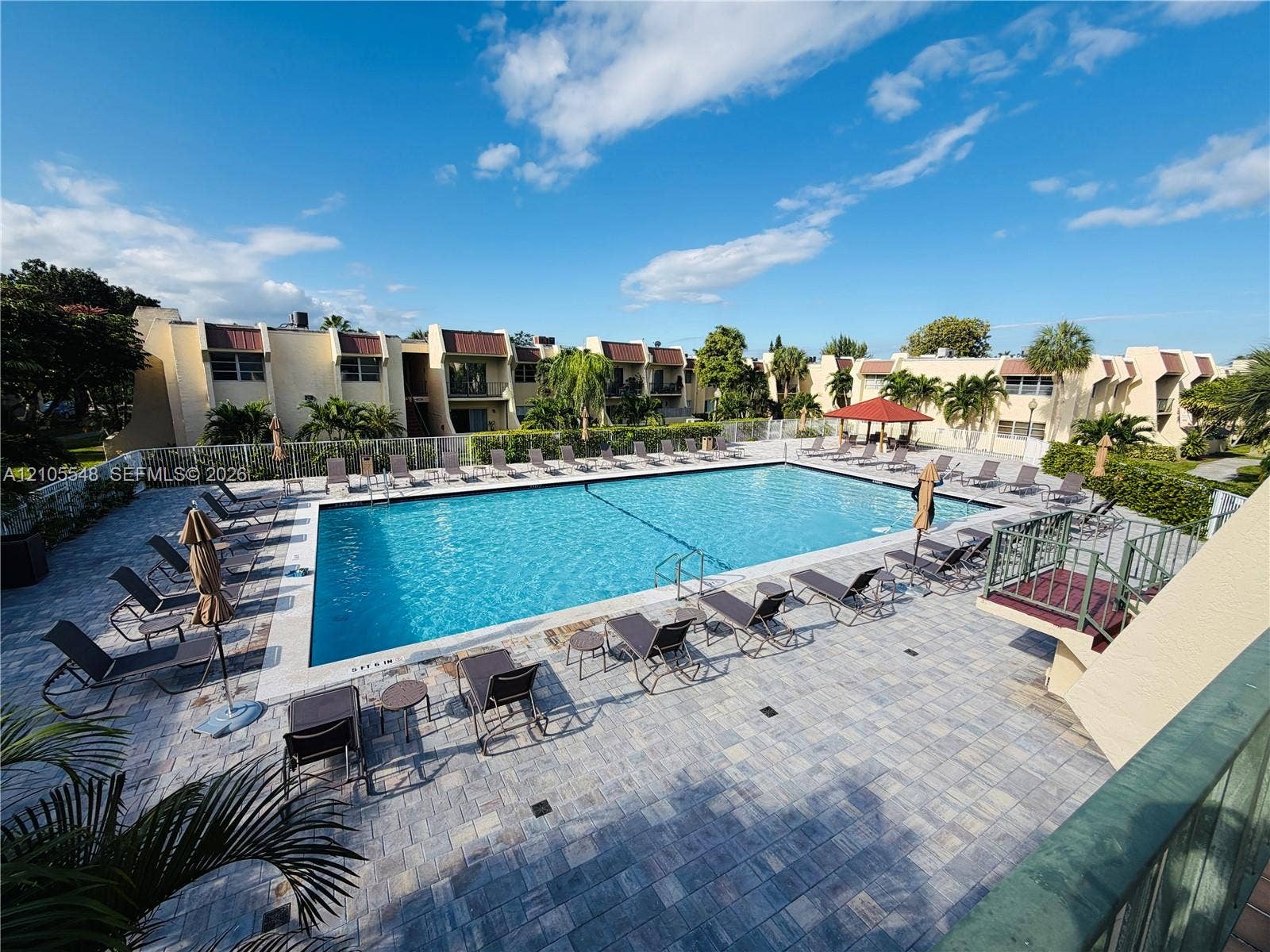 In-ground swimming pool with a stone paver deck, perimeter fencing, and a shaded pavilion