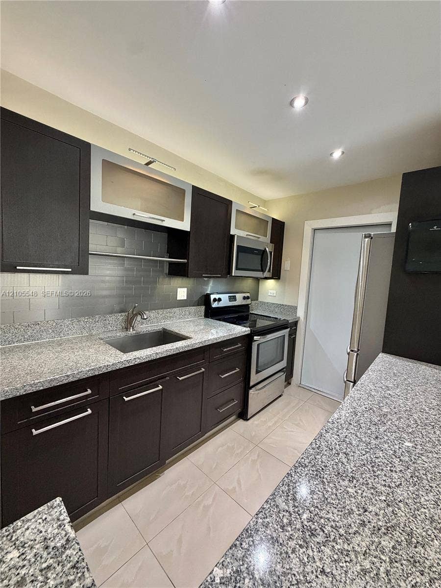 Kitchen featuring modern cabinetry, stone-finish countertops, subway tile backsplash, stainless steel appliances, and large-format tile flooring