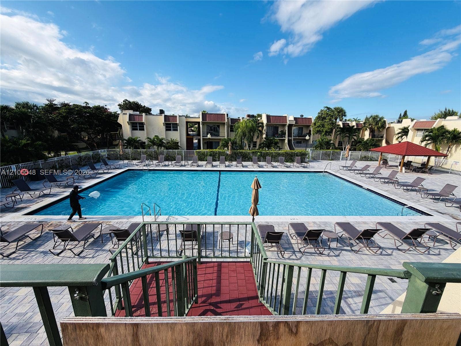 Community swimming pool with a paved deck, perimeter fencing, and a covered pavilion