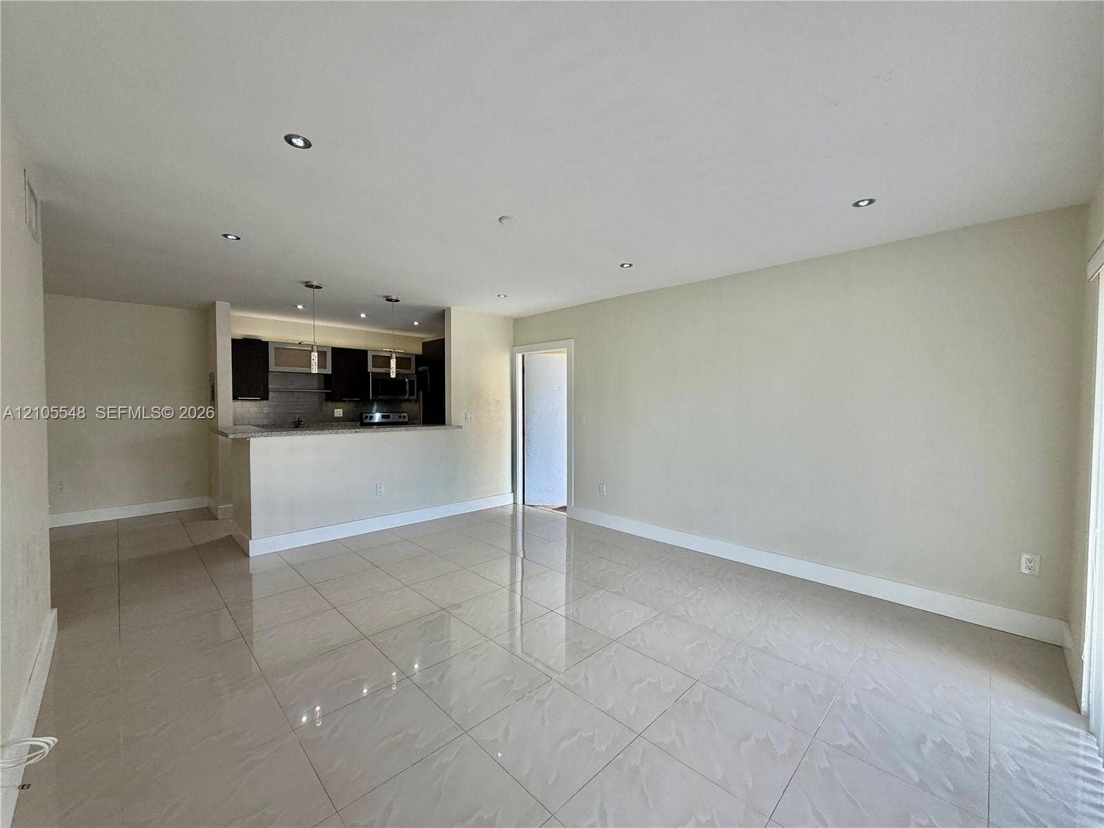 Open-concept interior featuring large-format porcelain tile flooring, recessed lighting, and kitchen with modern cabinetry, countertop peninsula, and pendant lighting