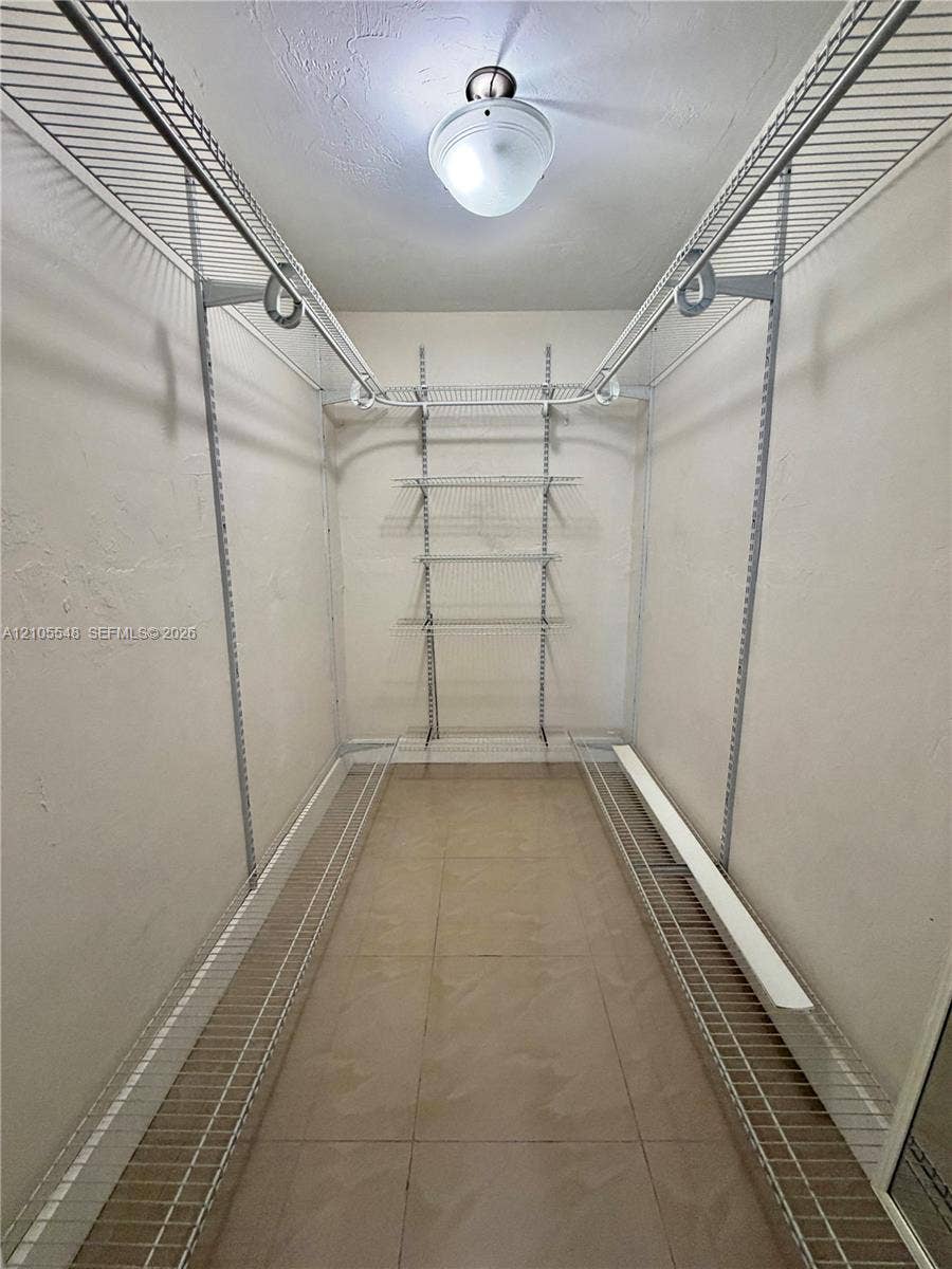 Walk-in closet in Primary bedroom, featuring tile flooring, white wire shelving, dual hanging rods, and a ceiling-mounted light fixture