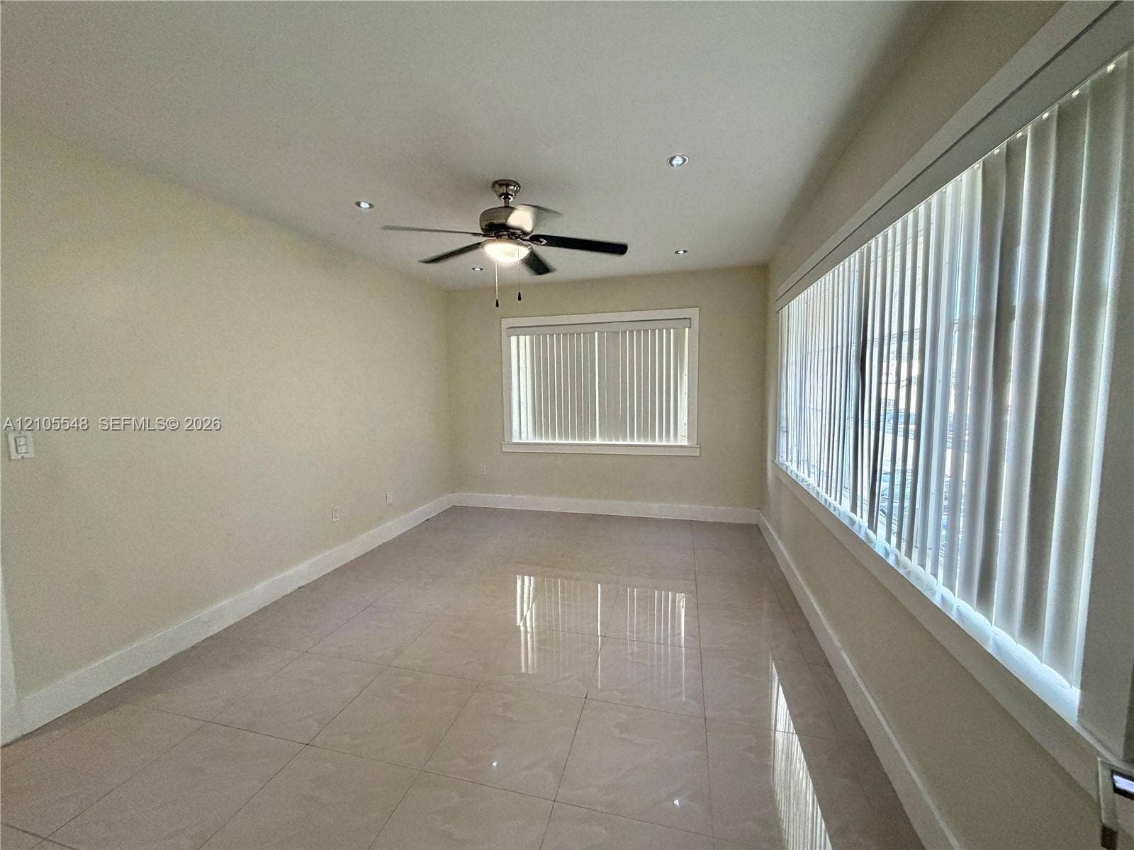 Neutral-toned interior featuring large-format porcelain tile flooring, recessed ceiling lighting, a central ceiling fan, and extensive windows dressed with vertical blinds