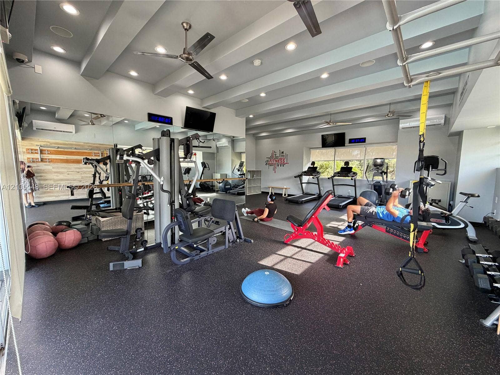 Gym featuring rubber flooring, recessed ceiling lighting, beam-style architecture, wall-to-wall mirrors, and dual ceiling fans