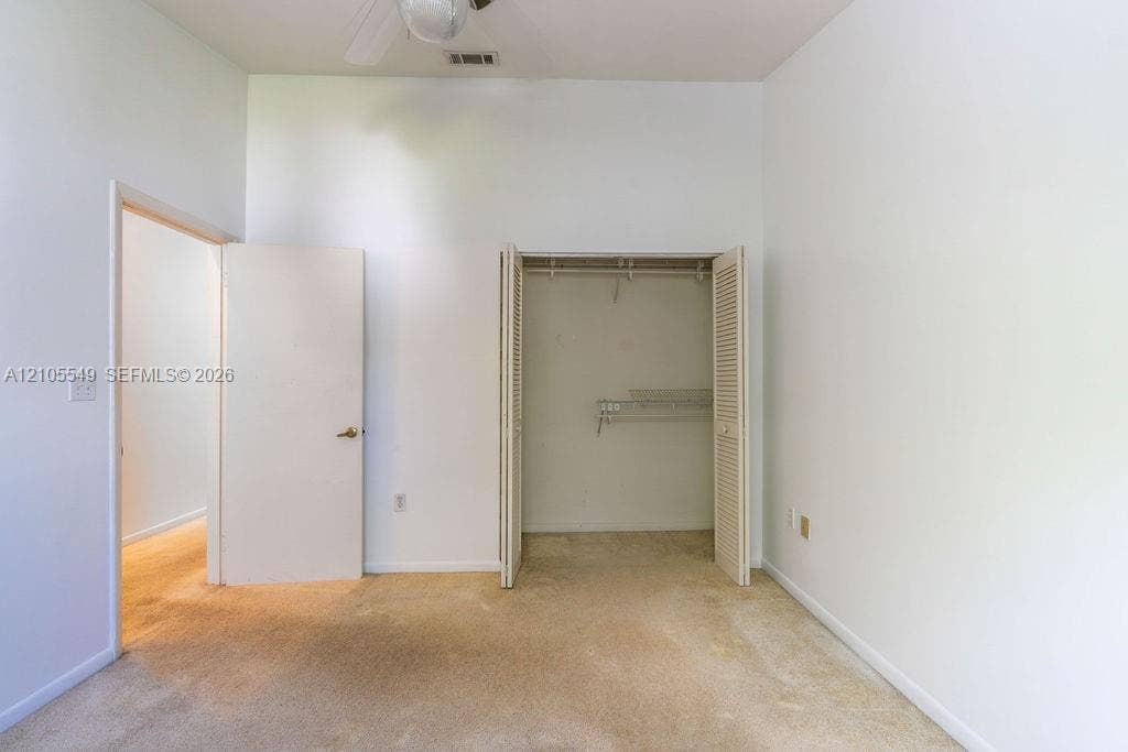 Neutral wall finishes, carpeted flooring, a ceiling-mounted fan, an open closet with bi-fold doors, and wire shelving