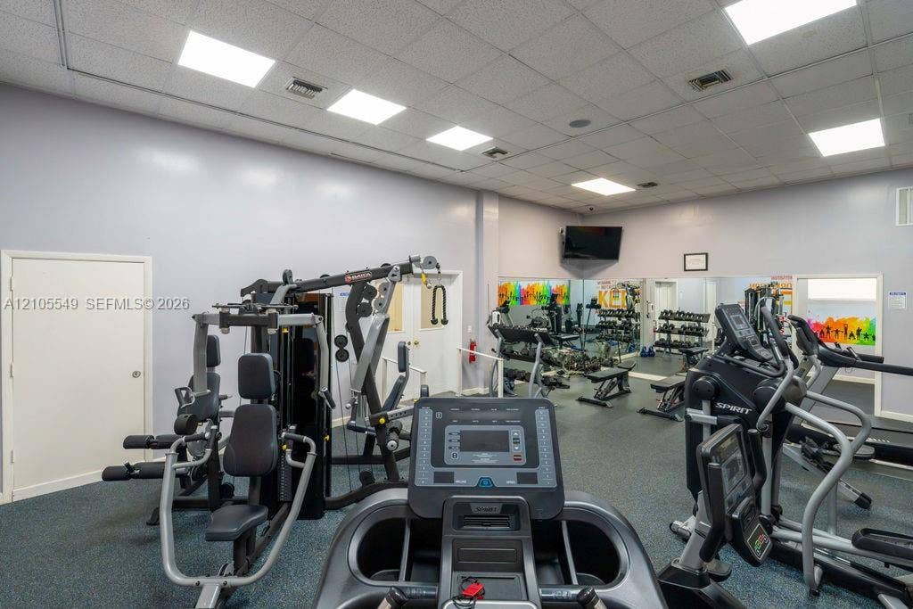 Dedicated fitness area featuring gym equipment, resilient flooring, recessed lighting, and a wall-mounted display