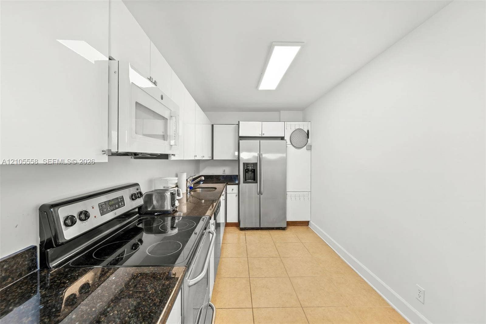 White cabinetry with integrated microwave, dark stone countertops, stainless steel refrigerator, and ceramic tile flooring