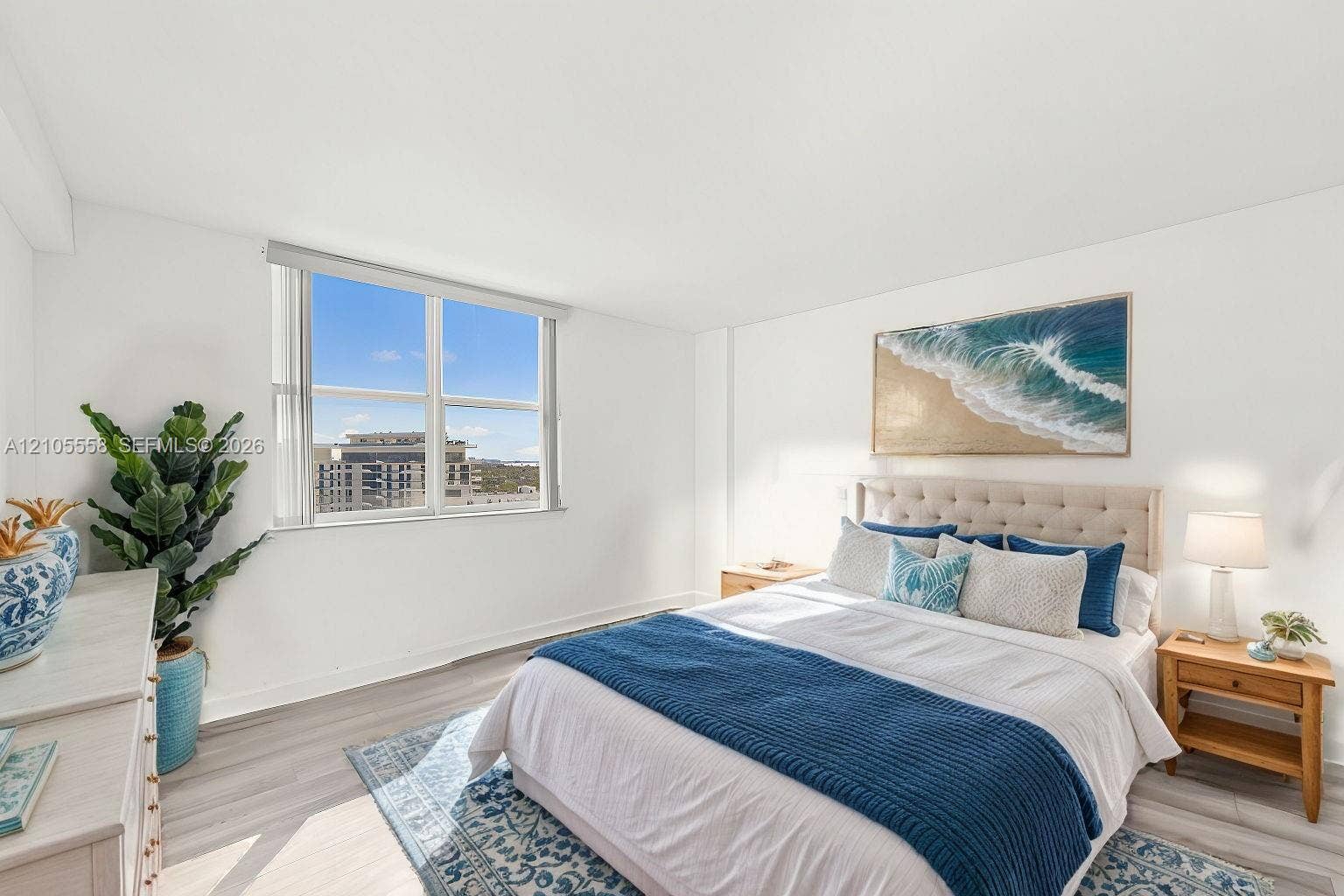 Expansive window with roller shade, neutral wall paint, light wood-finish flooring, and a tufted headboard