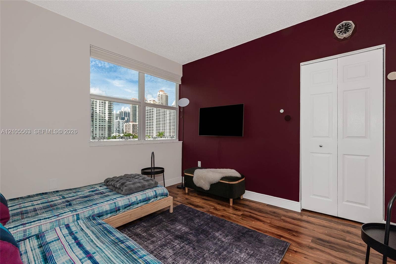 17145 N Bay Road, #4613, Sunny Isles Beach, Sunny Isles Beach, FL 33160 Expansive window with urban building scenery, wood-finish flooring, two-panel bifold closet doors, and a wall-mounted television