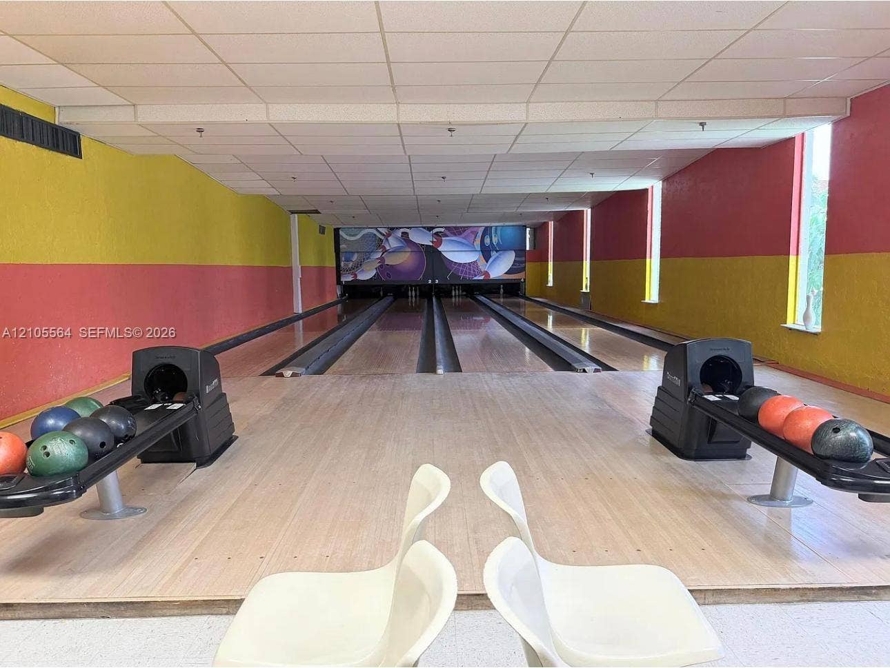 Two-lane bowling alley with light-toned wood-finish flooring, drop ceiling, and integrated ball returns