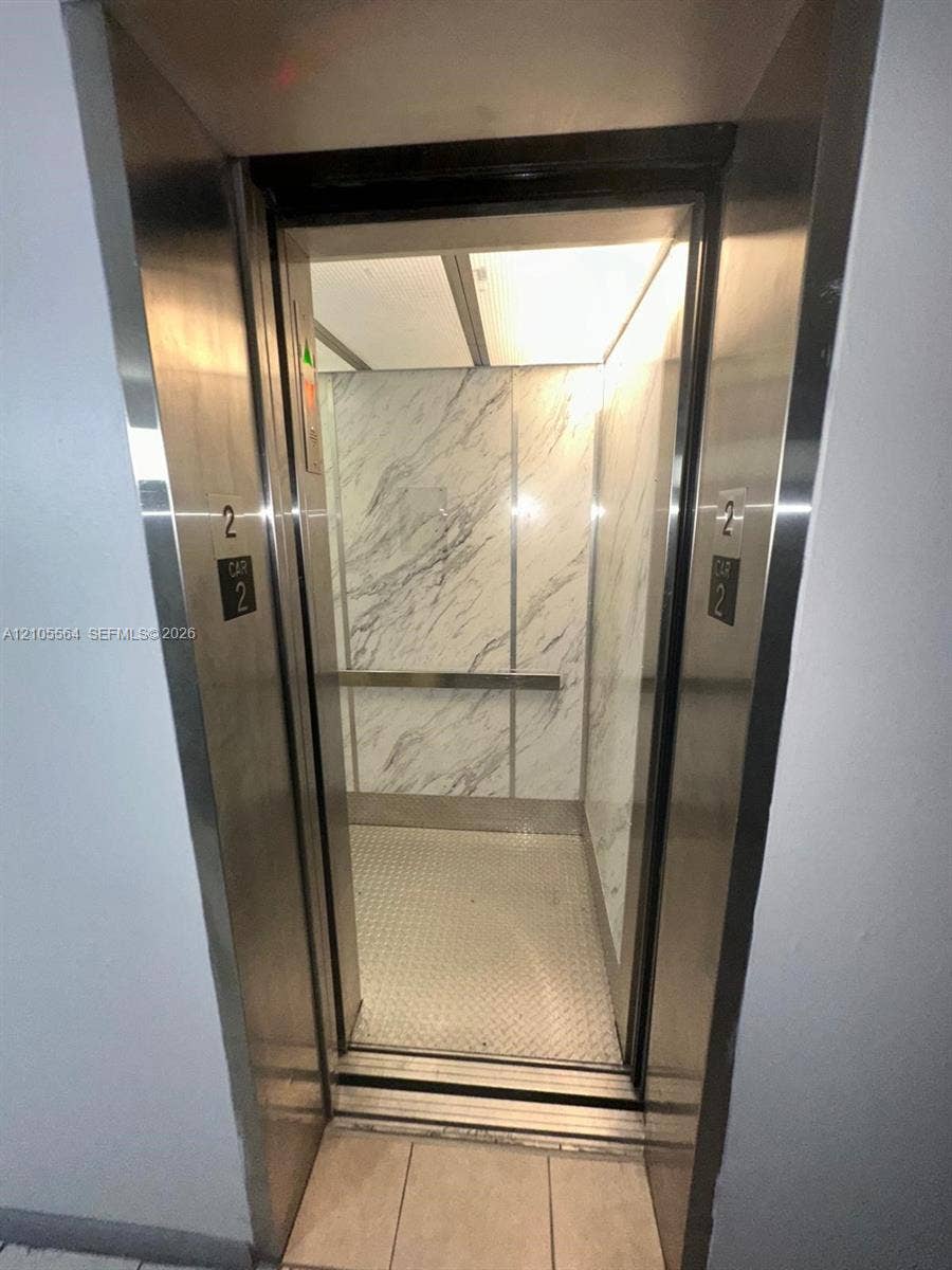 Stainless steel elevator with a marble-finish interior, a diamond plate floor, and a metal handrail